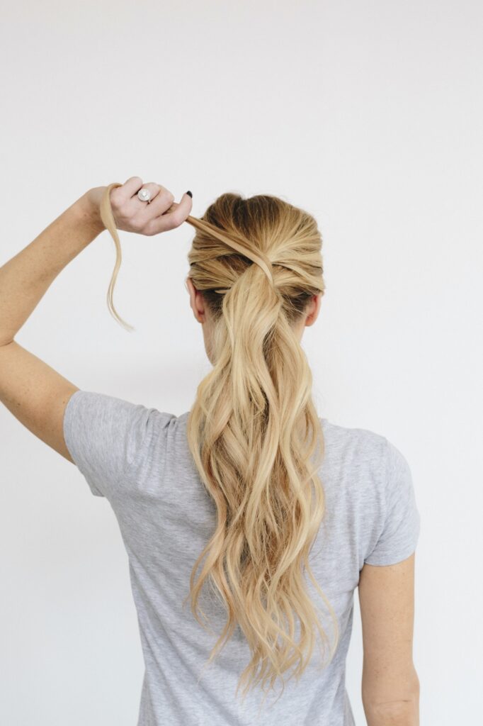 A young woman with long blond wavy hair. Tying a ponytail. Back view.