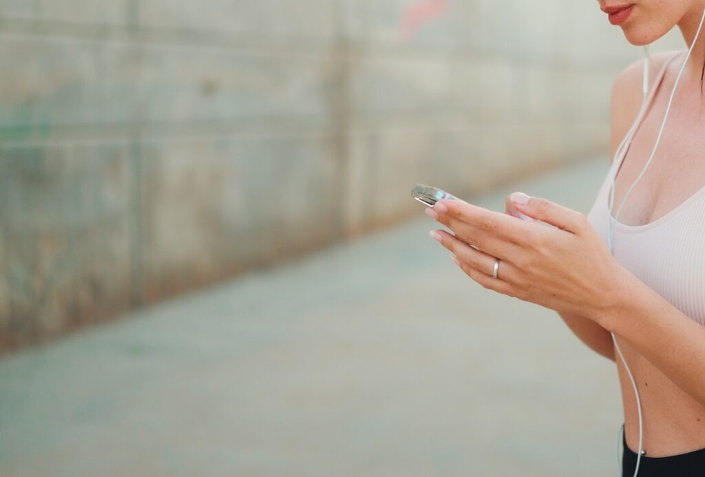 Young athletic woman in wired headphones, stands with mobile phone in her hands